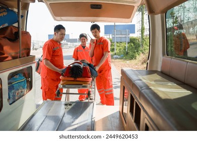 Group of paramedic or emergency medical technician (EMT) in an orange uniform places a neck and head accident victim on a bed in an ambulance. Urgent assistance during road accident.