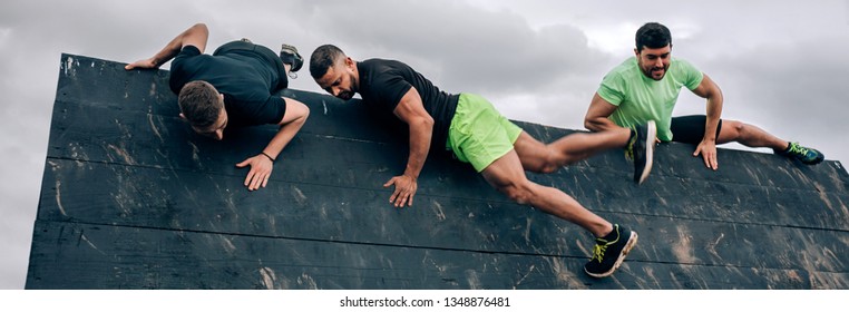 Group of participants in an obstacle course climbing an inverted wall - Powered by Shutterstock