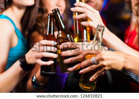 Group of party people - men and women - drinking beer in a pub or bar