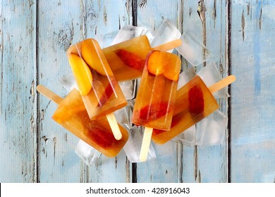 Group of peach iced tea popsicles with ice on a rustic blue wood background