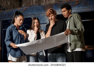 group of pensive young multicultural friends solving quest task while looking at map in escape room