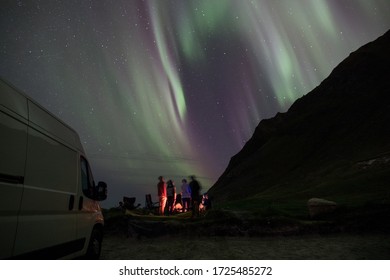 A Group Of People Around A Bonfire Under The Northern Lights. 