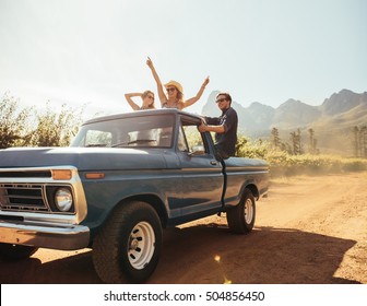 Group of people at the back of a pick up truck having fun. Young men and women enjoying on a road trip in countryside on a sunny day. - Powered by Shutterstock