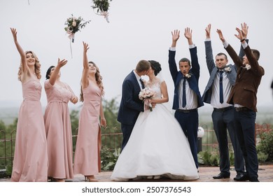 A group of people are celebrating a wedding, with the bride and groom in the center. The bride is wearing a white dress and the groom is wearing a suit. The group is standing on a hill - Powered by Shutterstock