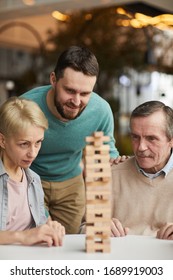 Group Of People Concentrating On The Game They Looking At Heap Of Wooden Details And Playing In Jenga Together