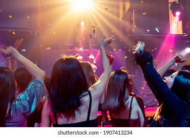 Group of people dance in disco night club to the beat of music from DJ on stage . New year night party and nightlife concept .