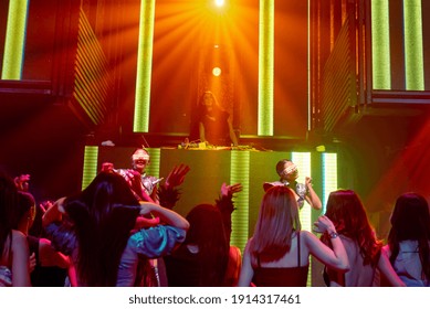 Group Of People Dance In Disco Night Club To The Beat Of Music From DJ On Stage . New Year Night Party And Nightlife Concept .