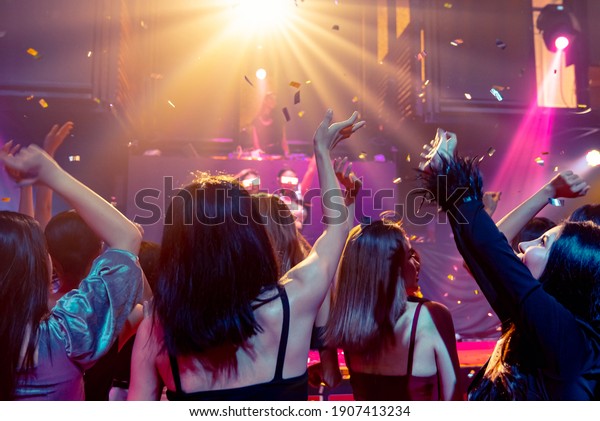 Group of people dance in disco night club to the beat\
of music from DJ on stage . New year night party and nightlife\
concept .