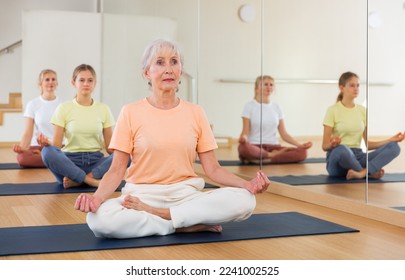 Group of people of different ages sitting in lotus position practicing meditation in yoga class - Powered by Shutterstock