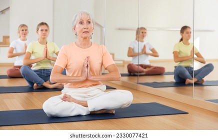 Group of people of different ages sitting in lotus position practicing meditation in yoga class - Powered by Shutterstock