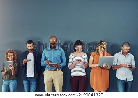 A group of people distracted due to the overuse of technology against gray studio background. Many employees are addicted and obsessed with social media with a dependence on gadgets or devices