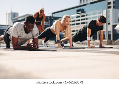 Group of people doing core exercise on fitness mat outdoors. Athletic group training together in the city. - Powered by Shutterstock