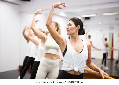 Group of people doing exercises using barre in gym with focus to kazakh woman in .foreground in health and fitness concept