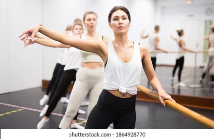 Group of people doing exercises using barre in gym with focus to fit athletic toned .woman in foreground in health and fitness concept