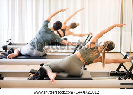 Group of people doing the mermaid pilates exercise or side stretch to tone the intercostal muscles viewed from the rear