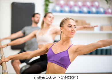 Group of people doing spinal twist exercises using the barre in a gym with focus to a fit athletic toned woman in the foreground in a health and fitness concept