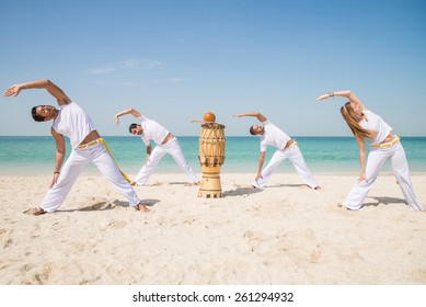 Group of people doing stretching - Capoeira team training on the beach - Martial arts athletes performing stunts
