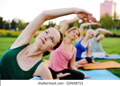 Group Of People Doing Yoga On The Green With Fresh Grass Outdoors. Healthy Lifestyle