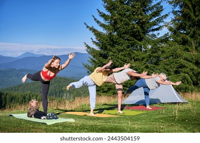 Group of people doing yoga pose outdoor in camping in the mountains. Adults and children standing on yoga mats, each doing yoga pose under clear blue sky in morning. - Powered by Shutterstock