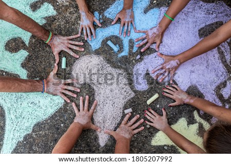 A group of people drawing with colored chalks on the floor with his hands in the street a map of the world