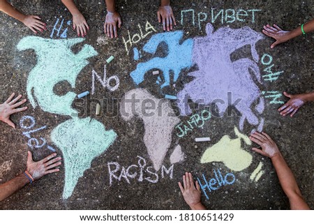 A group of people drawing with colored chalks on the floor with his hands in the street a map of the world with words 