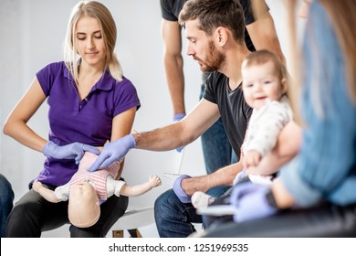 Group Of People During The First Aid Training With Instructor Showing On Manikin How To Do Artificial Respiration For The Baby