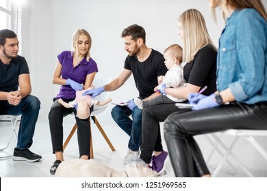 Group Of People During The First Aid Training With Instructor Showing On Manikin How To Do Artificial Respiration For The Baby