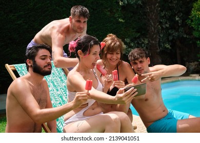 Group of people eating strawberry popsicles and taking a selfie sitting on the grass near by a swimming pool. - Powered by Shutterstock