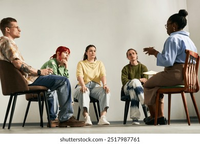 Group of people engaging in group therapy session led by therapist sitting in circle in cozy room with relaxed atmosphere, discussing personal issues and seeking support from each other - Powered by Shutterstock