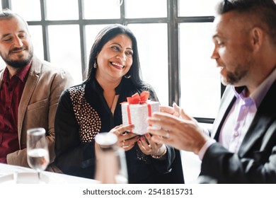 Group of people exchanging gifts at a celebration. Smiling woman receiving a present. Joyful atmosphere with friends sharing gifts and happiness. People exchanging holiday gifts. - Powered by Shutterstock