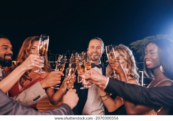 Group of people in\
formalwear toasting with champagne and smiling while spending time\
on luxury party