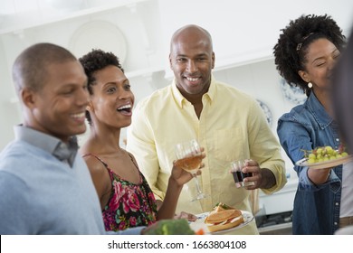 A group of people gathering for a party and a meal. An informal office party or networking social event. People handing plates of food across a buffet table.