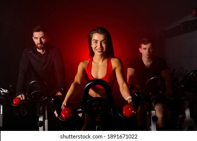 Group Of People In The Gym, Exercising Their Legs Doing Cardio Training, Having Spinning Class At Gym In Dark Neon Lighted Smoky Space