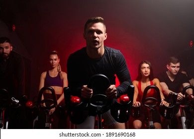 group of people in the gym, exercising their legs doing cardio training, having spinning class at gym in dark neon lighted smoky space