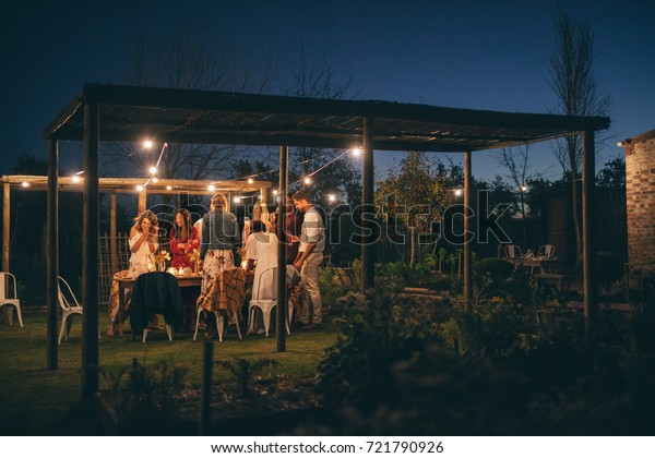 Group of people having a\
dinner party. Men and women standing around a table in garden\
restaurant .