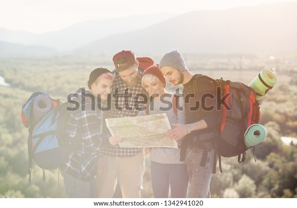 Group of people hiking and looking at map during\
their adventure. Two men and two women, hikers exploring mountains.\
Happy friends with backpacks using map to choose right direction.\
Travel concept.