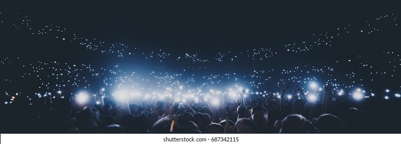 Группа людей, держащих зажигалки и мобильные телефоны на концерте 
толпа людей силуэты с поднятыми руками. Темный фон, дым, прожекторы. Яркий свет