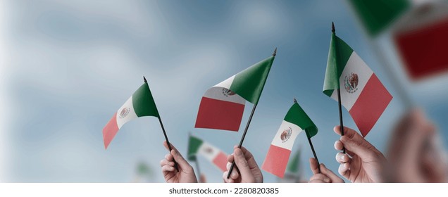 A group of people holding small flags of the Mexico in their hands.