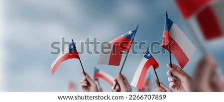 A group of people holding small flags of the Chile in their hands.