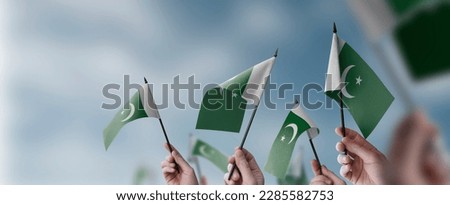 A group of people holding small flags of the Pakistan in their hands.