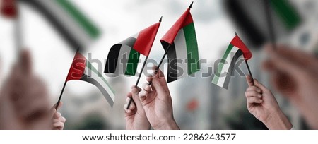A group of people holding small flags of the Arab Emirates in their hands.