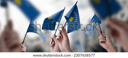 A group of people holding small flags of the Kosovo in their hands.