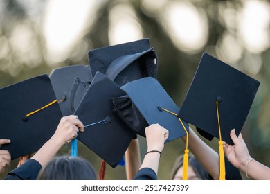 A group of people are holding up their graduation caps. The caps are black and yellow, and the people are smiling. Scene is celebratory and happy, as the graduates are proud of their accomplishments - Powered by Shutterstock