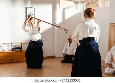 A group of people, including martial arts instructors, are standing in a room, demonstrating Jo wooden staff techniques in front of students. Text: "Aikido" - Powered by Shutterstock