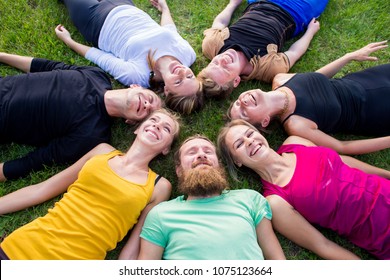 A group of people lies on a green grass in a circle
