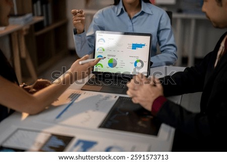 A group of people are looking at a computer screen with graphs and charts. They are discussing the data and making decisions based on the information. Scene is focused and serious
