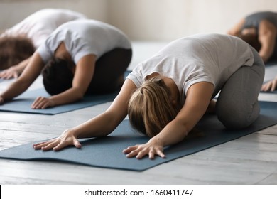Group of people lying on mats performing Child Pose close up focus on caucasian woman. Participants beginners rest after work out in sport club studio, reduces stress and fatigue, yoga session concept