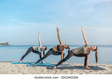 Group of people making yoga pose on beach near water. Young female athletes sportswomen exercising outdoors, stretching arms and legs, warming-up before training together. - Powered by Shutterstock