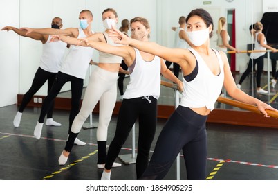 Group of people in masks doing exercises using barre in gym during coronavirus .pneumonia outbreak