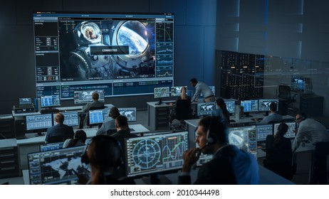 Group Of People In Mission Control Center Establish Successful Video Connection On A Big Screen With An Astronaut On Board Of A Space Station. Flight Control Scientists Sit In Front Computer Displays.